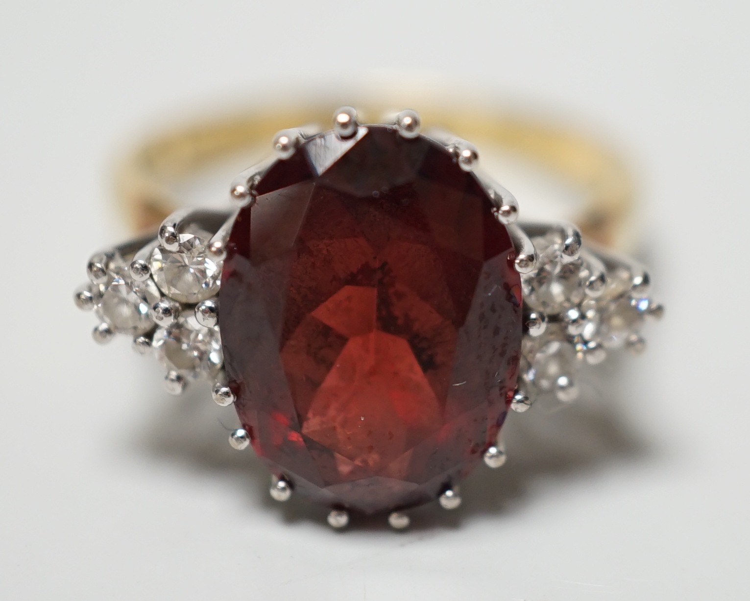 A modern 18ct gold and oval cut garnet set dress ring, with six stone diamond set shoulders, size M/N, gross weight 4.8 grams.